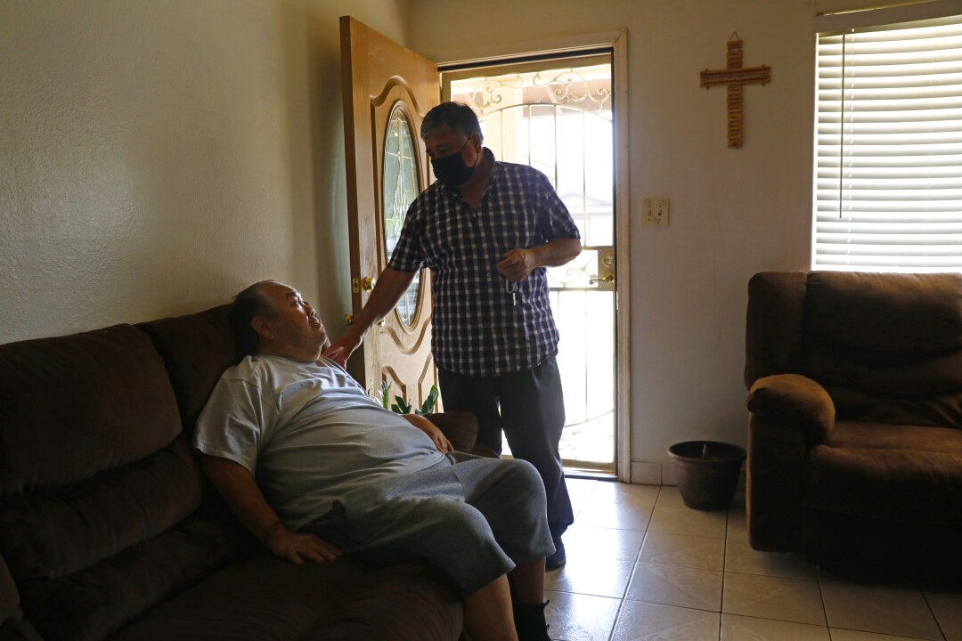 Jose Mireles, left, sits on a couch as Juan Flores, standing, touches his shoulder. 