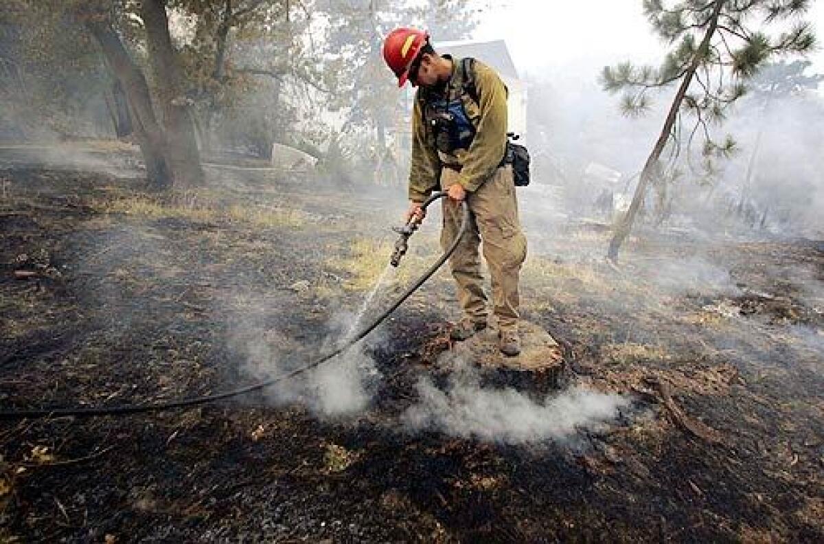 Standing on a tree stump, a fireman puts out hot spots in a residential area near Running Springs.