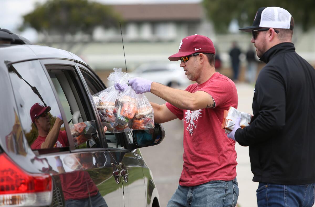 Andrew Walanski, left, and Tim Floyd, assistant principals at Ocean View and Huntington Beach high schools, respectfully, distribute "grab and go" student lunches as families drive up to Ocean View High on Friday.