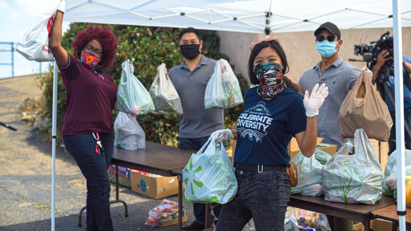 Photo of four people wearing face masks and holding grocery bags at a local food distribution event in South San Diego.