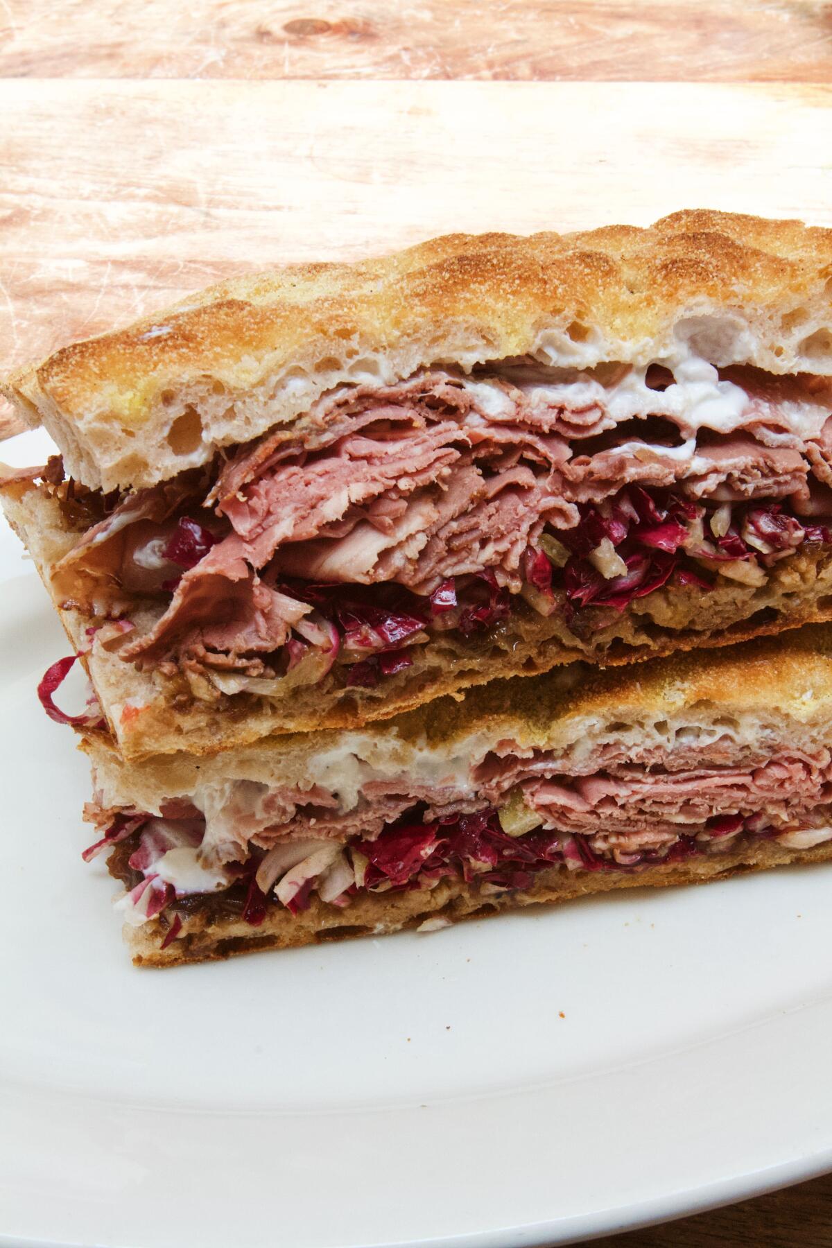 A vertical photo of a roast beef sandwich with radicchio on a white plate at Tre Mani and Ghisallo in Santa Monica.