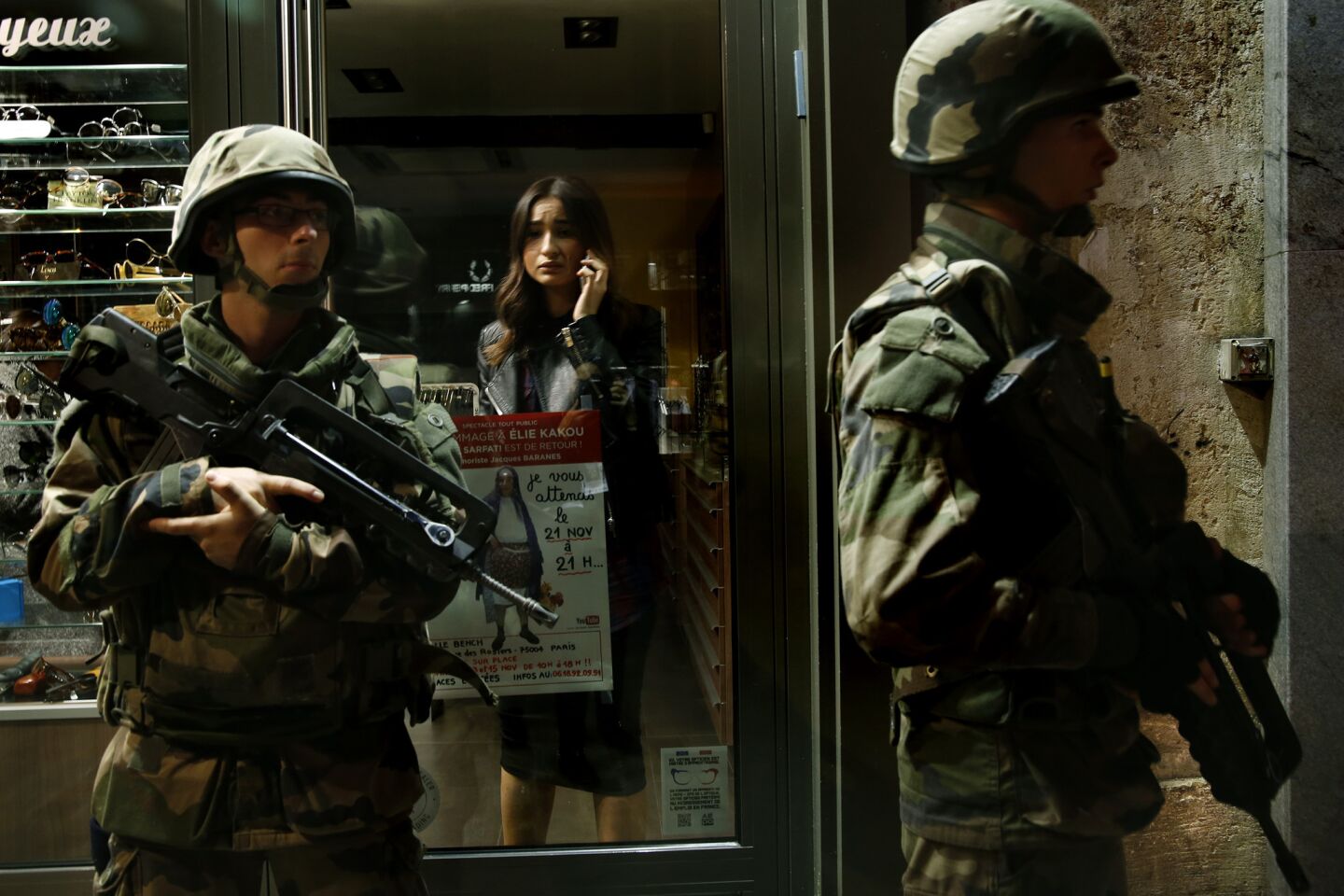 A Paris shopkeeper stays inside Sunday as soldiers guard the street where she works.