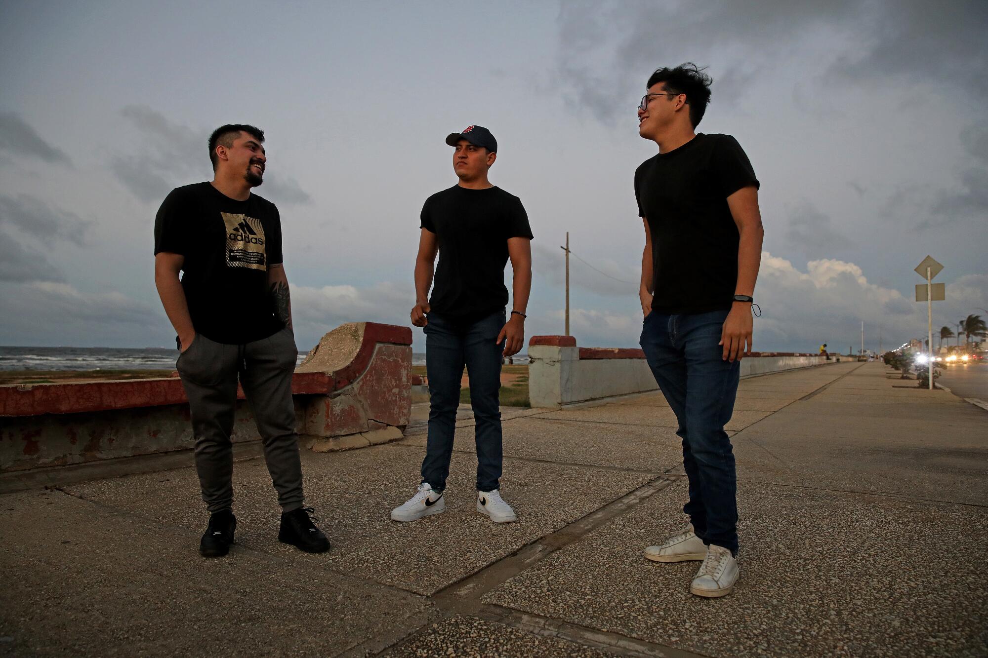 Three young men stand near the waterfront.