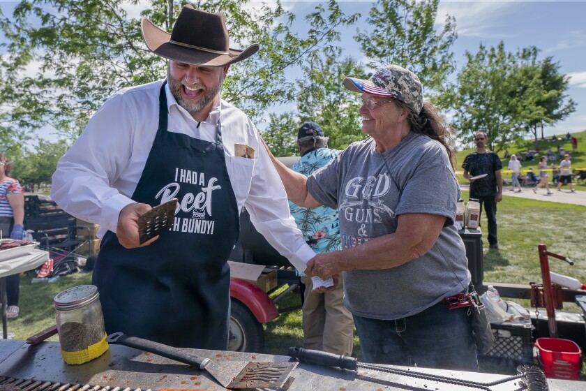 A woman pats Ammon Bundy on the back as he holds a spatula over a grill.