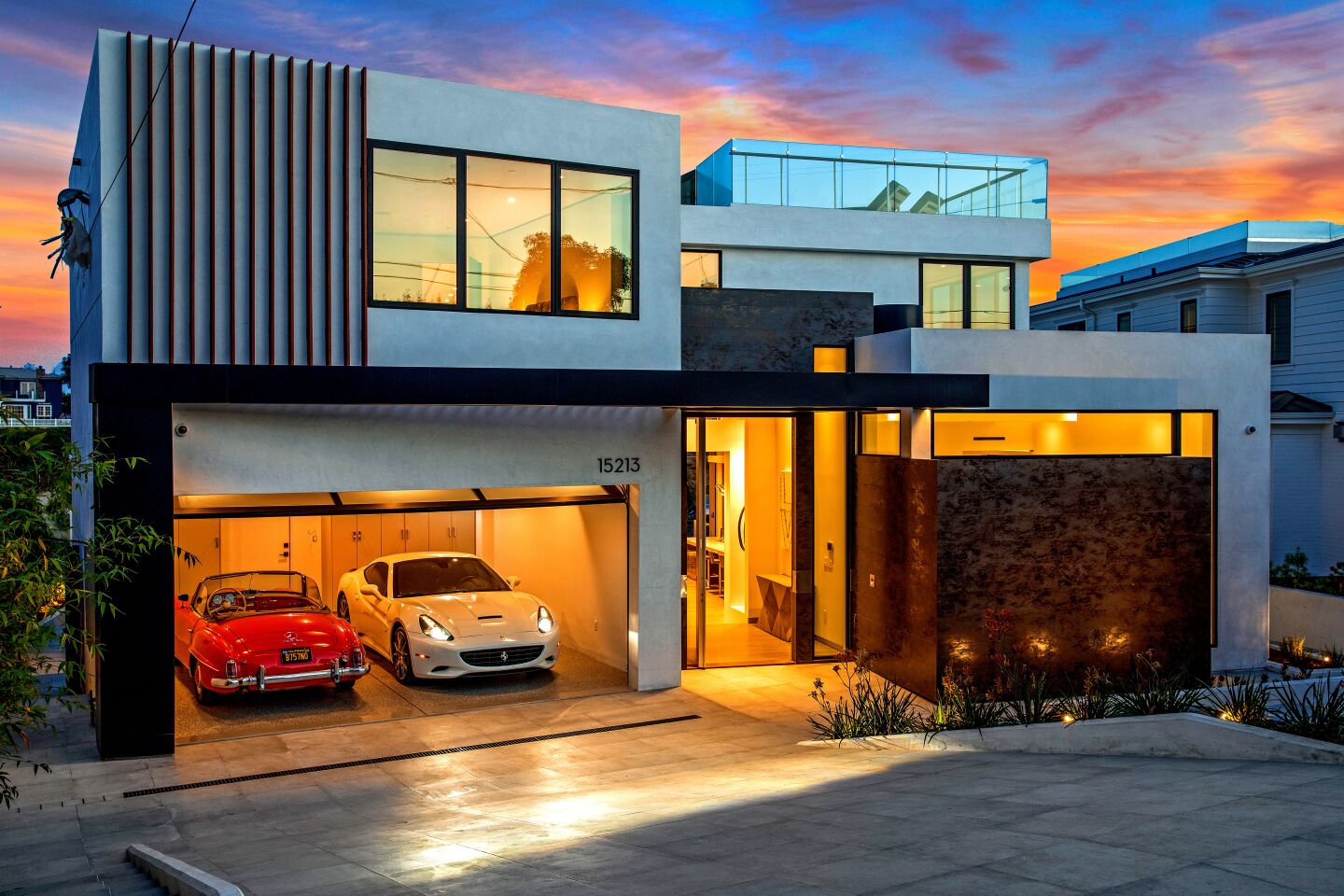 Two expensive cars sit in the lighted garage at the front of the home.
