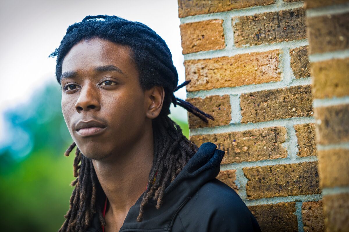 A Black man with dreadlocks, shown in front of a brick structure 