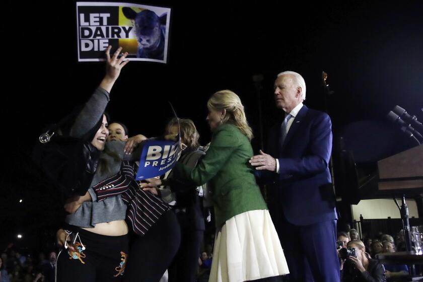 A protester at left, is held back by Biden adviser Symone Sanders, wearing stripes, face unseen, and Jill Biden, second from right, as Democratic presidential candidate former Vice President Joe Biden stands, at right, during a primary election night rally, Tuesday, March 3, 2020, in Los Angeles. (AP Photo/Marcio Jose Sanchez)