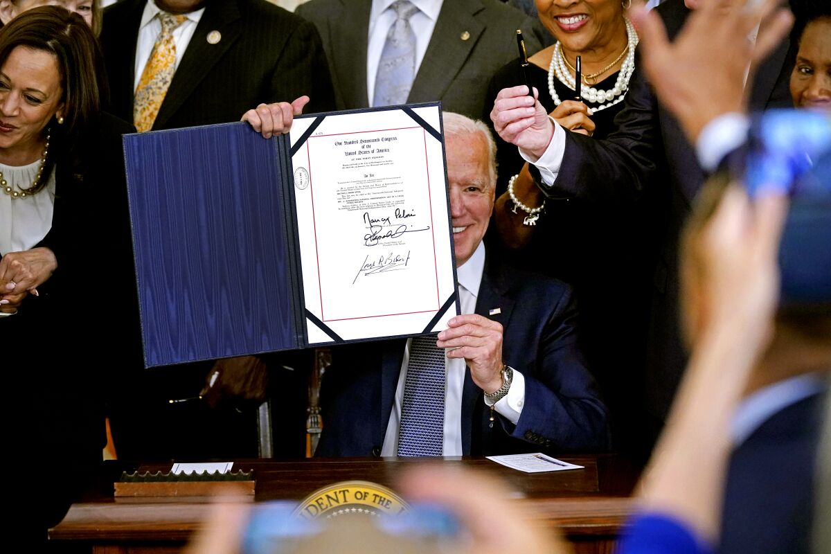 Biden is surrounded by people as he holds up the Juneteenth act in the White House