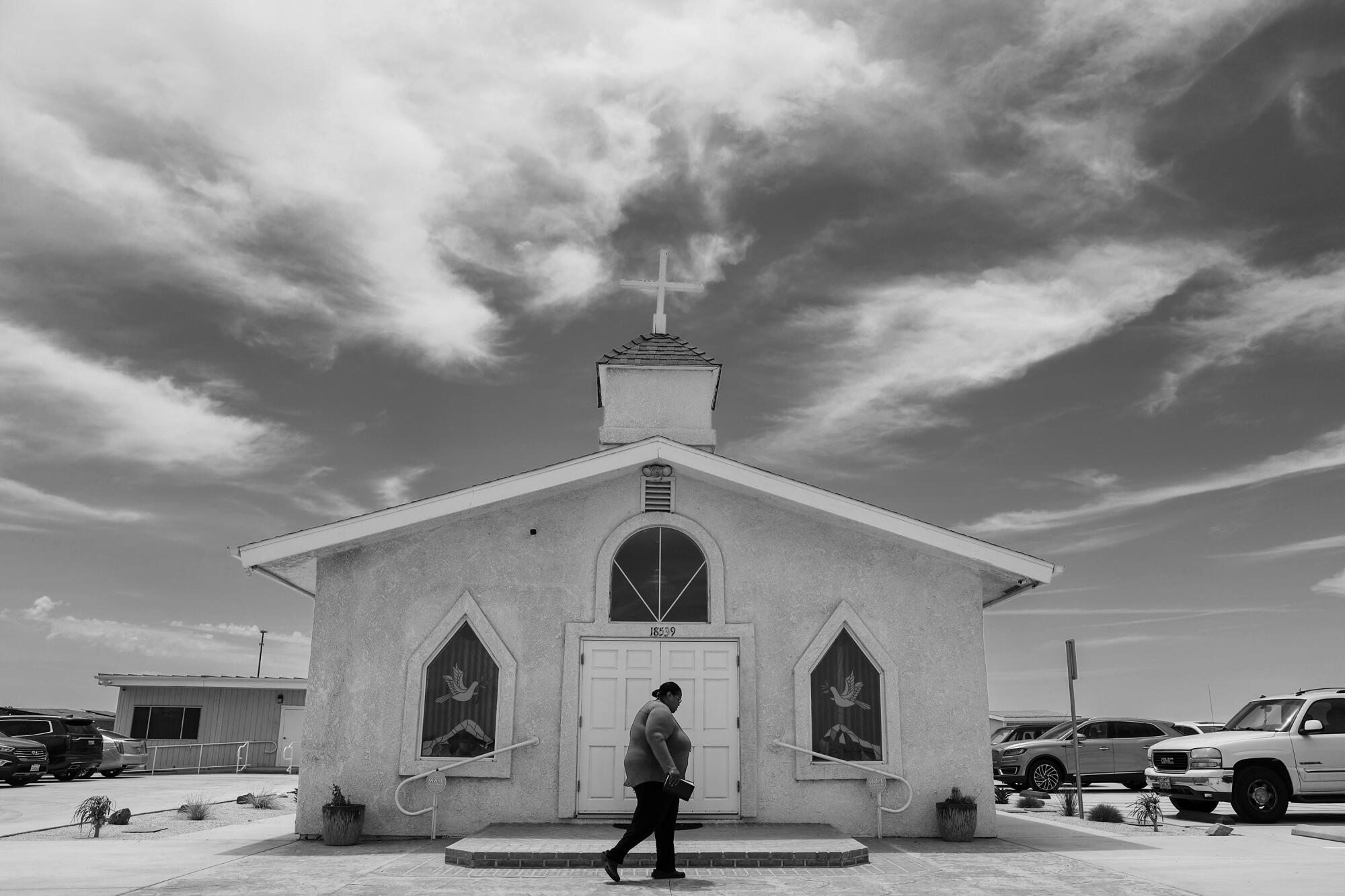 A person walks from a church toward parked cars.