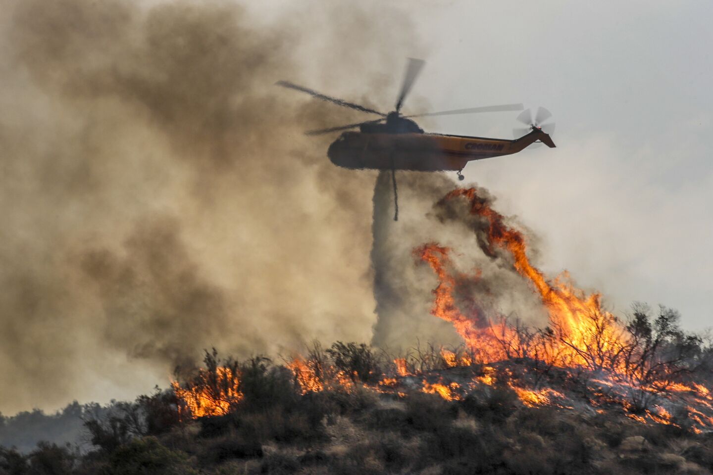 A helicopter makes a water drop on burning brush on a hill across from homes in Lake Elsinore.