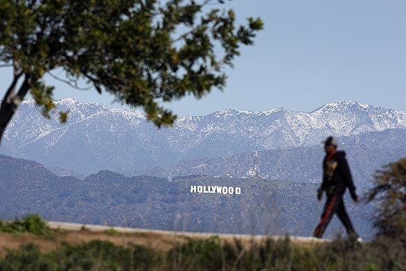 A man takes a scenic walk with a view of the Hollywood sign and Hollywood Hills at Kenneth Hahn State Recreation Area in Baldwin Hills, a favorite photography location for viewing the Los Angeles Basin and local mountains covered with snow.