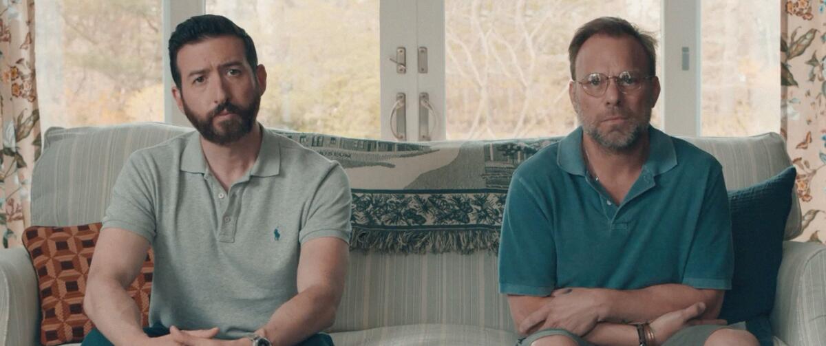 Two men sitting on a couch in the movie “Give or Take.”