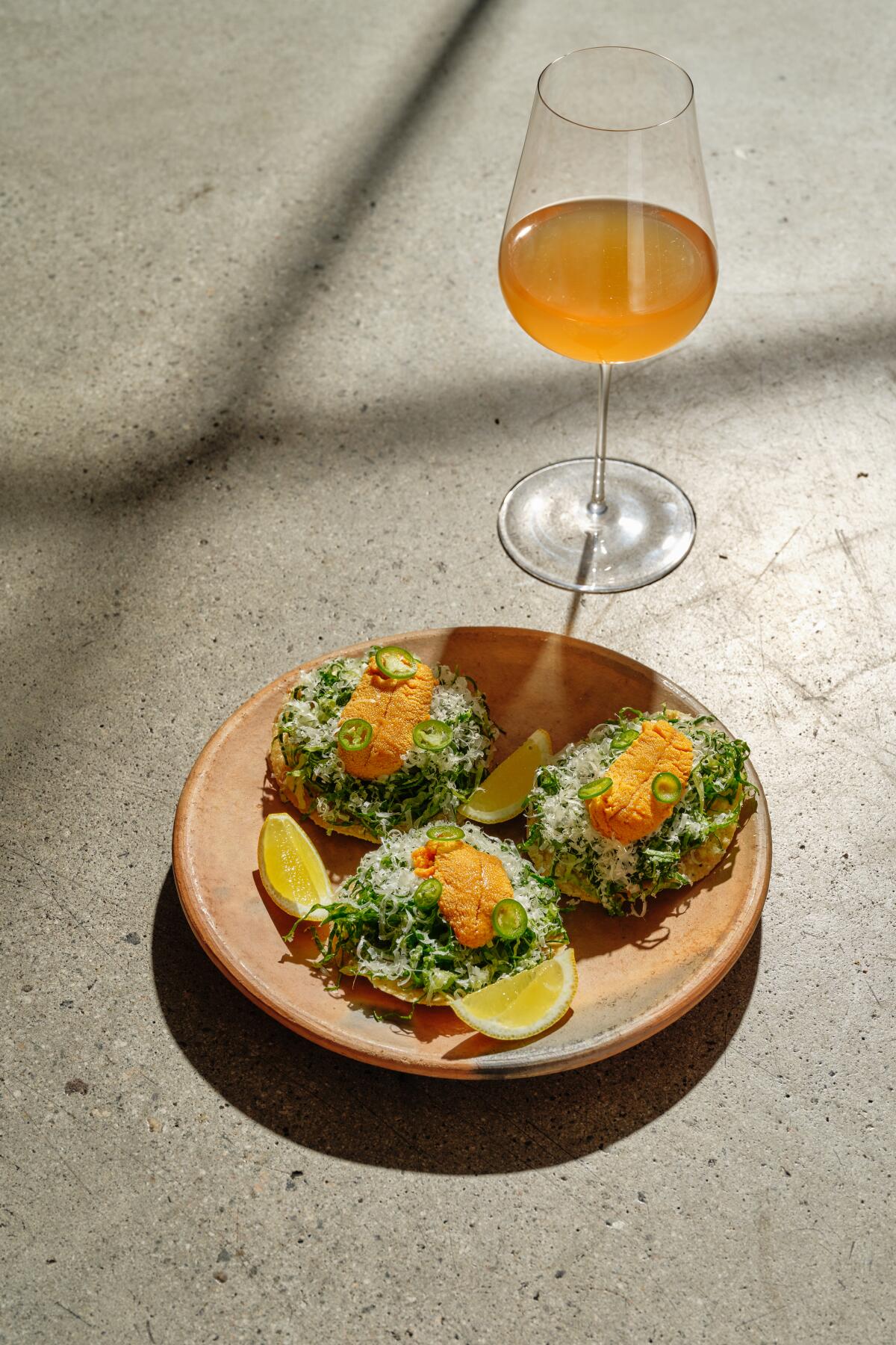 Uni tostada from Damian, served on a plate next to a wine glass holding an orange beverage.
