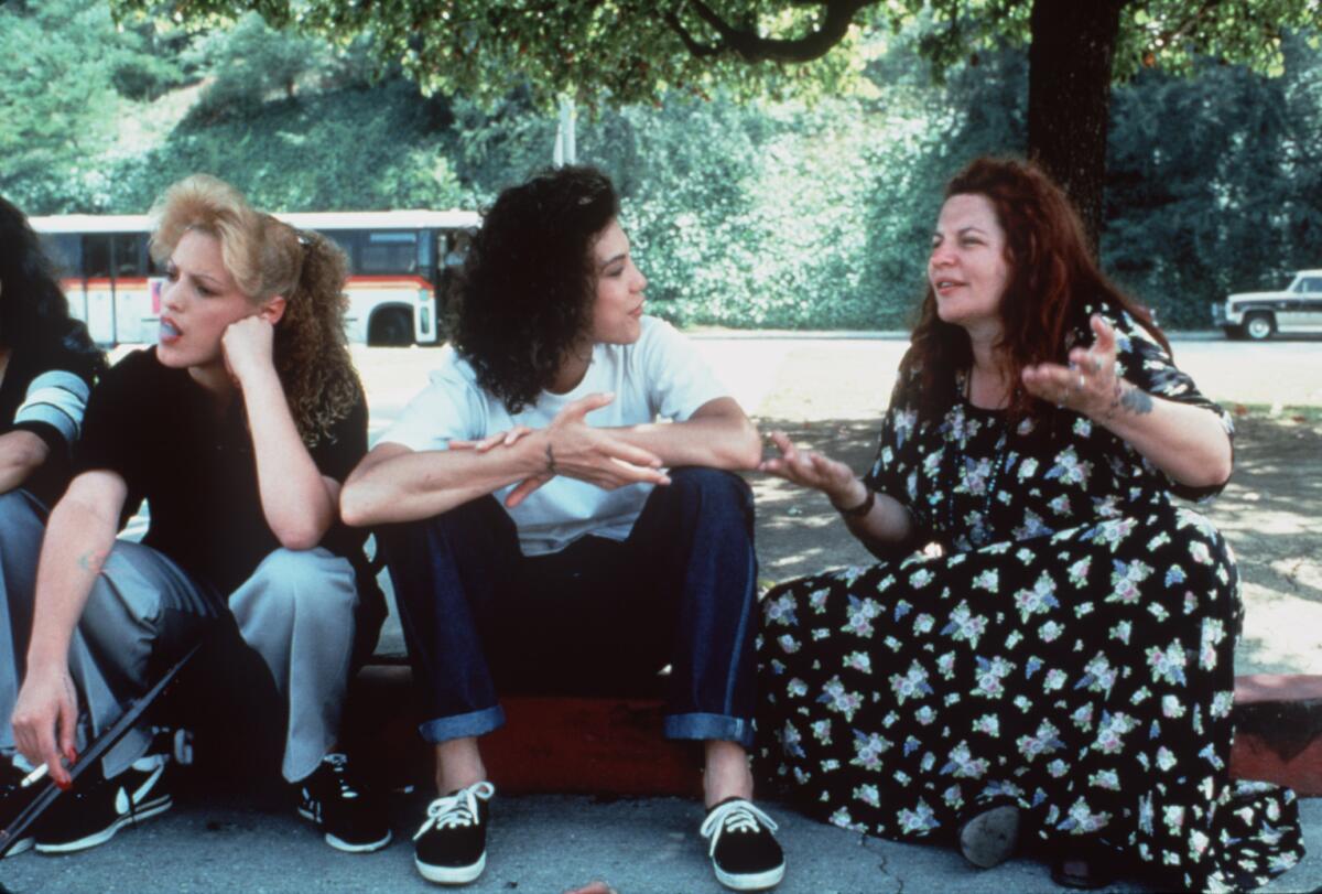 A director chats with her actors as they all sit on a curb.