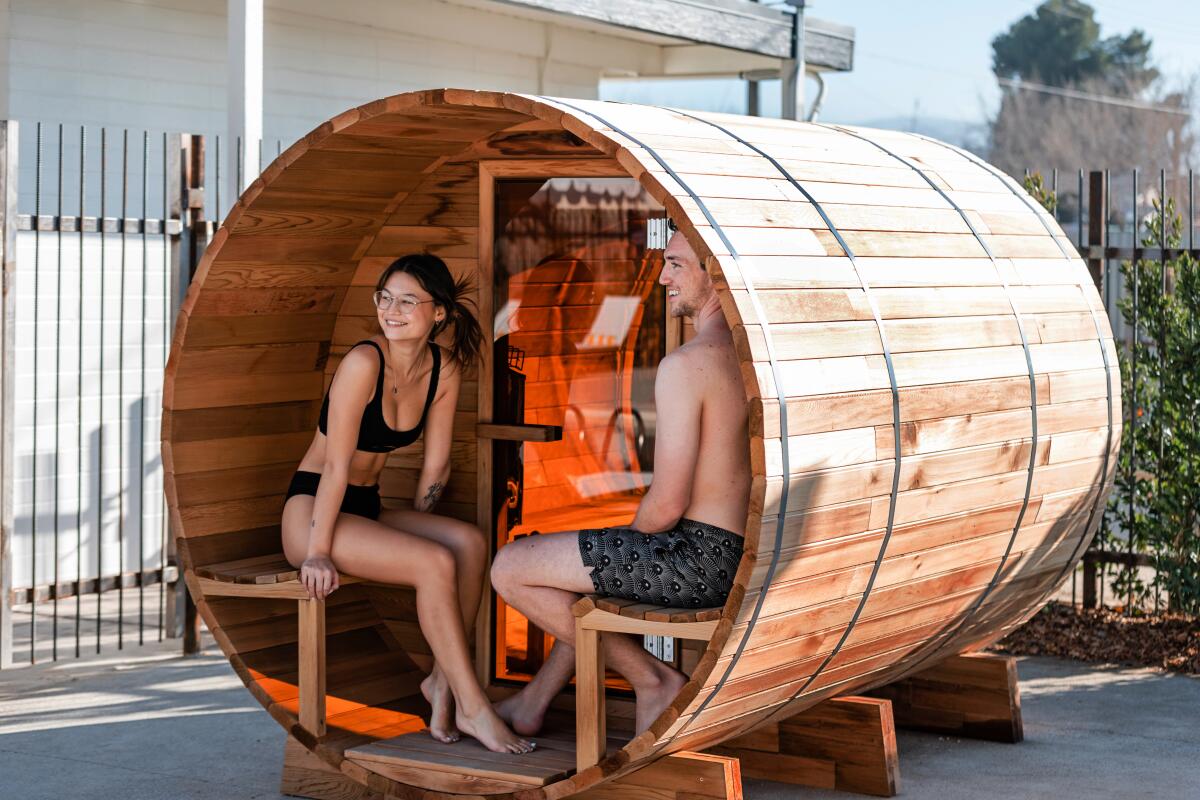 A couple sit in a sauna made from a barrel  