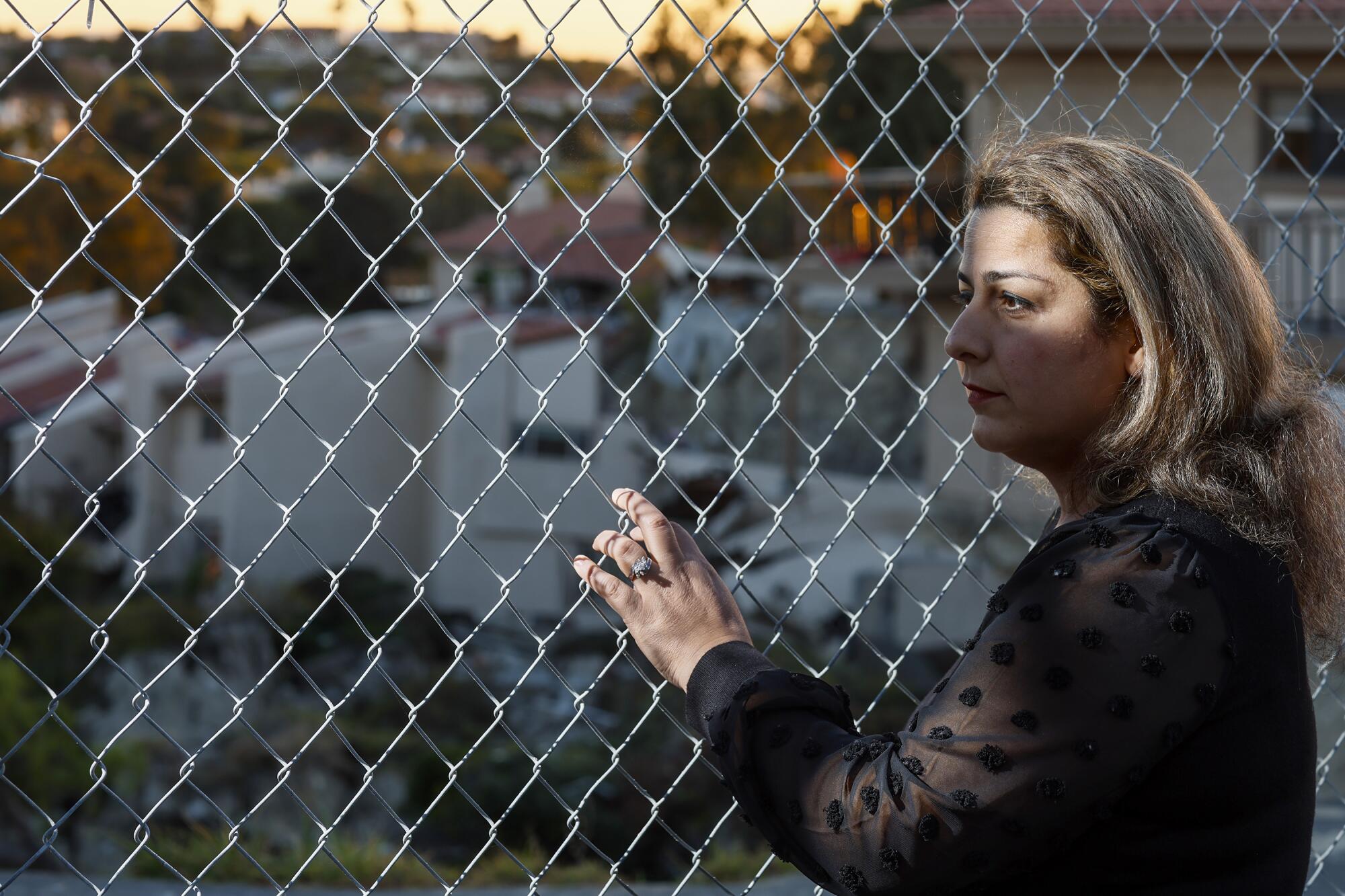 A woman holds onto a chain-link fence and looks into the distance.