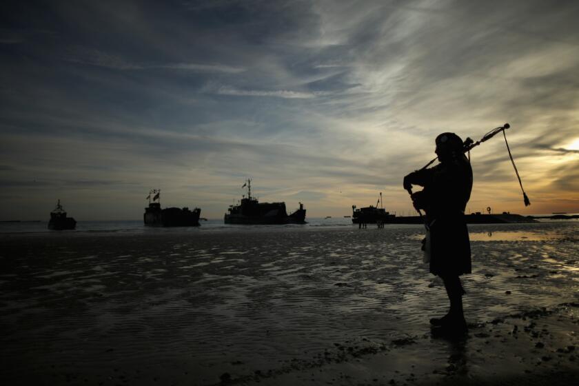 A piper plays a lament as British landing craft near shore at Gold Beach on Friday as part of 70th-anniversary observances of the D-Day invasion of Normandy.