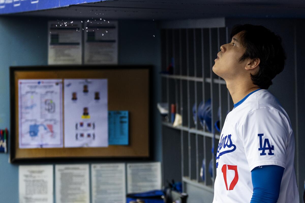 Dodgers star Shohei Ohtani stands in the dugout during a rain delay before Sunday's game.