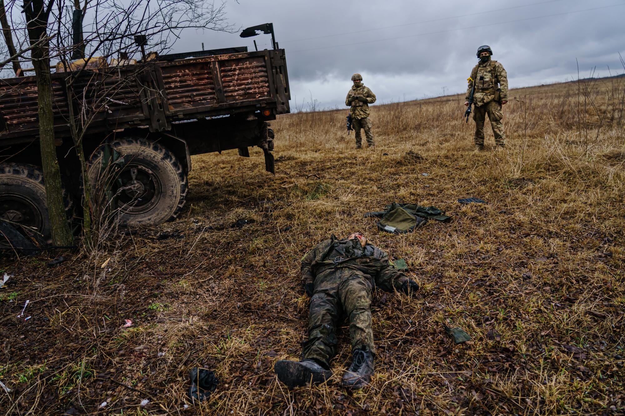 Soldiers stand near another soldier's body on the ground.