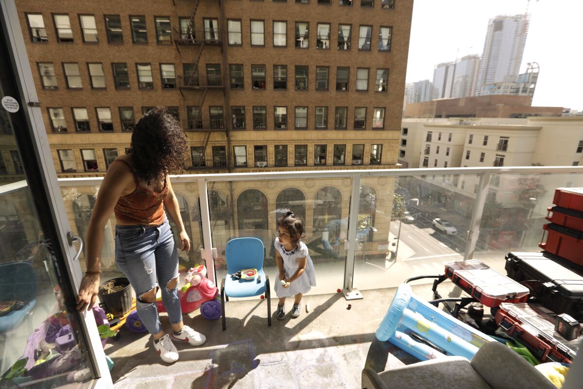 A young woman at left looks on at a toddler while she plays on the balcony of a hotel room