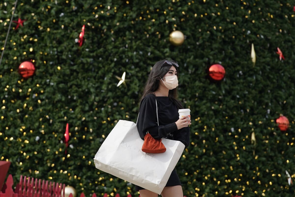 A woman wearing a mask passes in front of the annual Macy's Great Tree at Union Square in San Francisco.