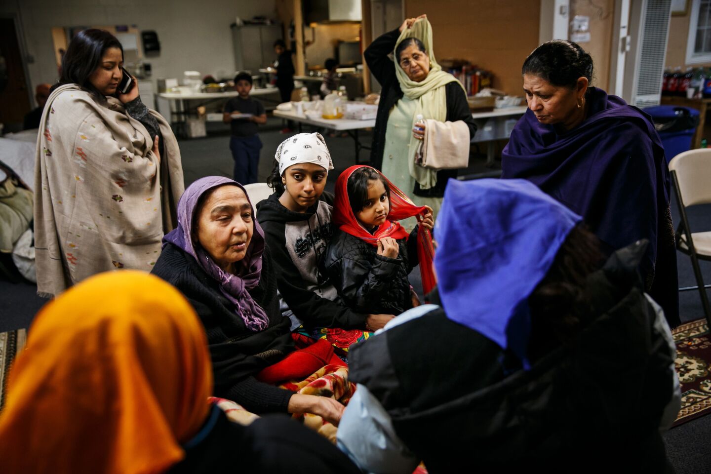 Kamlesh Nahar, from center left, Sunsagam Preet Kaur, 11 1/2, and Muskan Kaur, 5, listen to stories told by fellow evacuees as they settle in for the night at Shri Guru Ravidass.