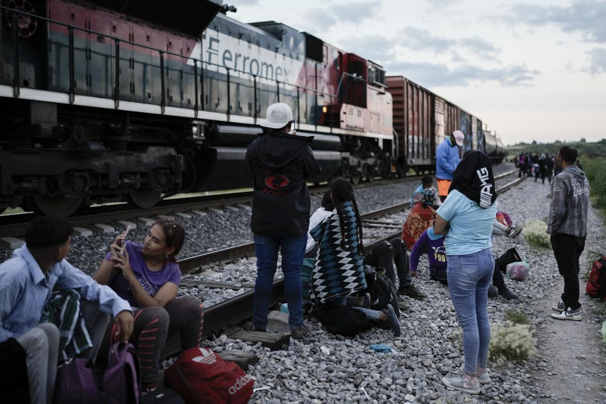 Migrantes observan un tren en marcha junto a las vías en las que esperan para subir a bordo 
