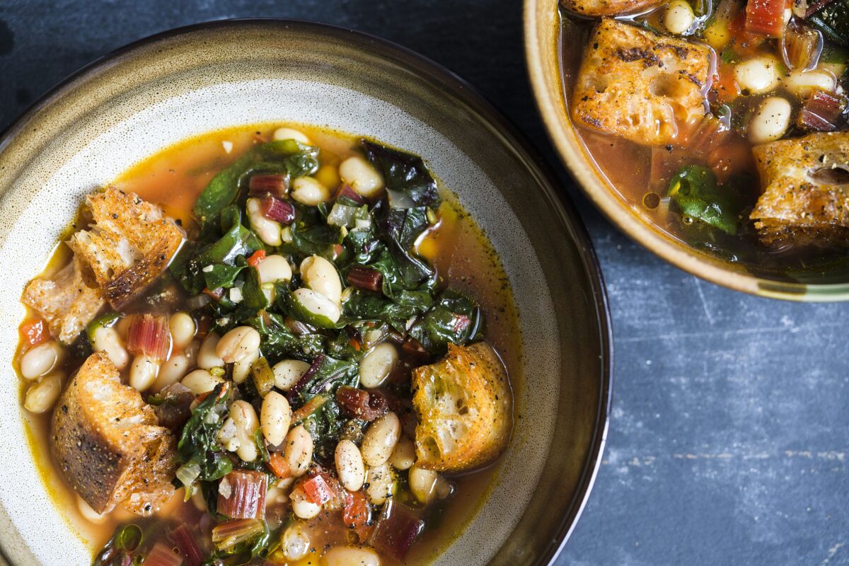 This image released by Milk Street shows a recipe for Tuscan Soup. Milk Street kitchens start from scratch with ciabatta croutons and canned white beans. Sturdy greens such as red-veined Swiss chard add color and texture from crispy stems. They are sautéed with onions and bell pepper. If you like, serve the soup topped with grated Parmesan cheese. (Milk Street via AP)