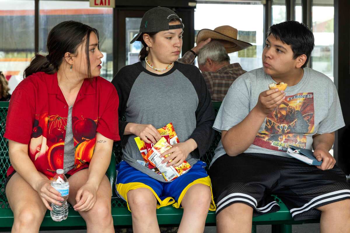 Three young people eat snacks on a bench