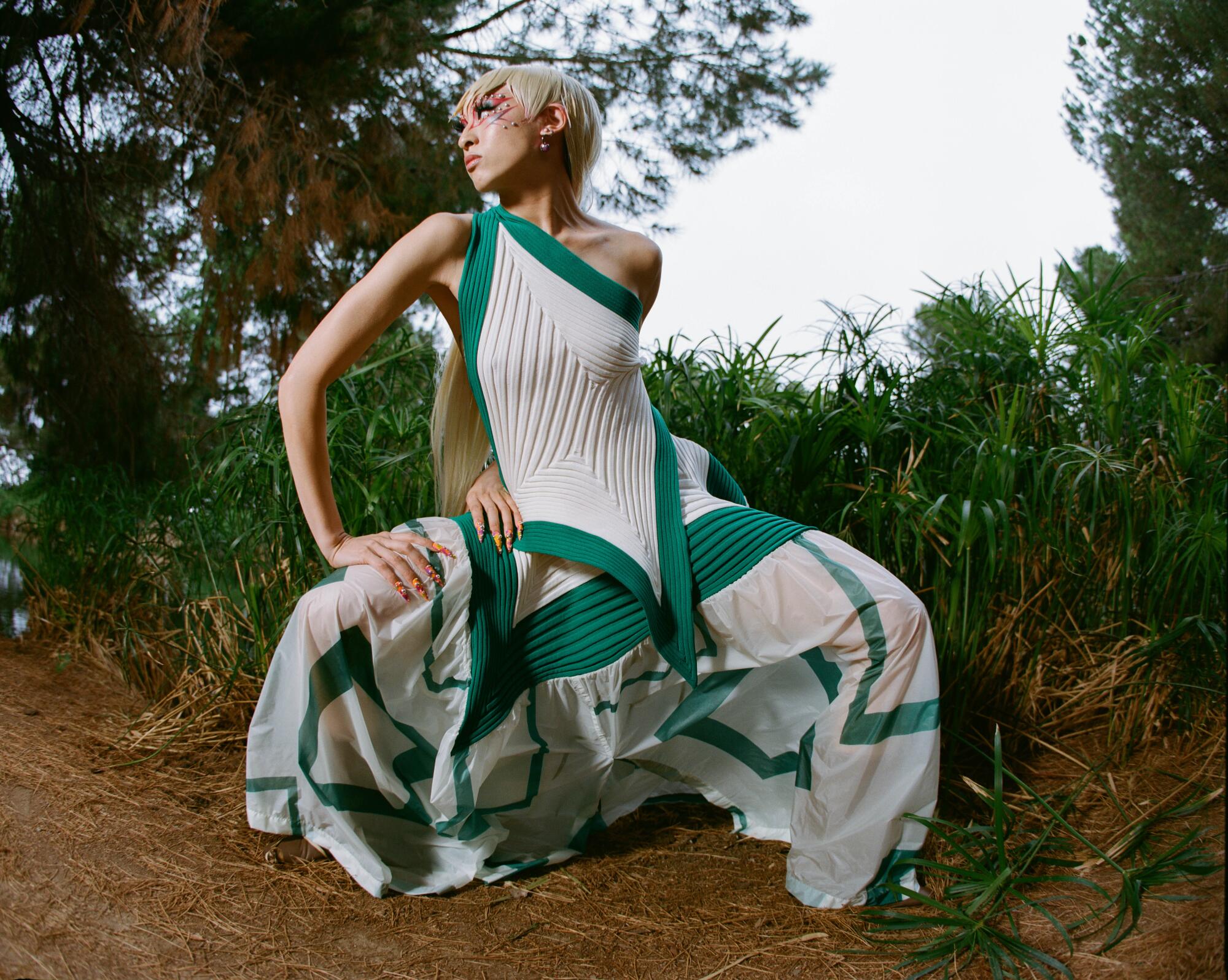 A model kneels outside in a white tank with green trim and a white skirt with green abstract stripes