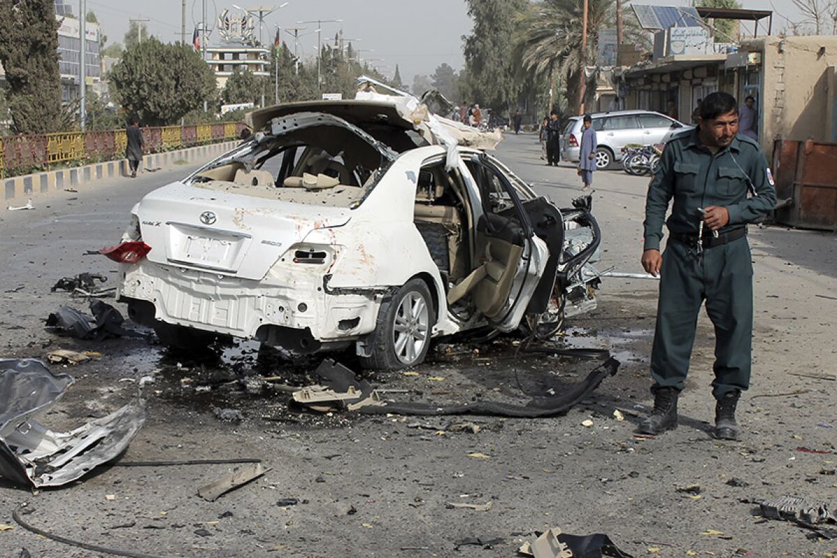 An Afghan policeman investigates a damaged car following a bomb attack in southern Helmand province on Thursday.