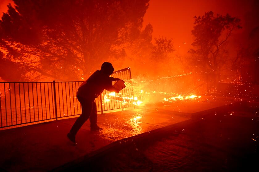 PORTER RANCH, CALIFORNIA OCTOBER 11, 2019-Ozzy Butler pours water on to his deck at his parents house as the Saddleridge Fire burns along Thunderbird Ave. in Porter Ranch Friday morning. (Wally Skalij/Los Angeles Times)