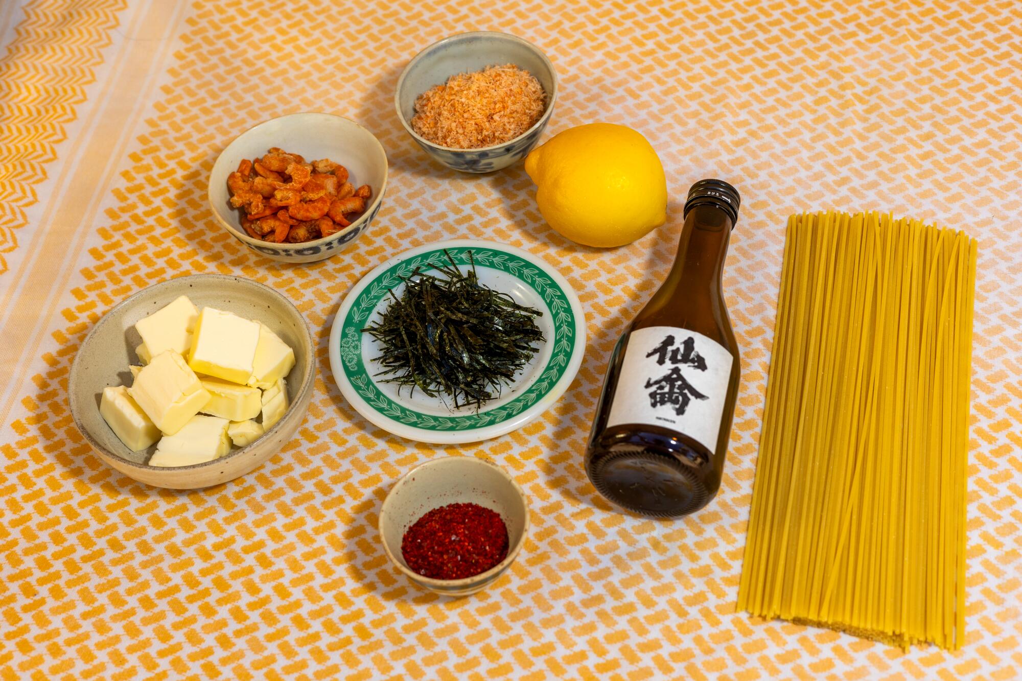 Small dishes of unsalted butter, chili powder, sake, dried shrimp and nori with a lemon, spaghetti and bottle of sake