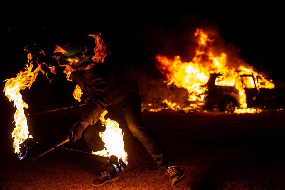 A man twirls a flaming baton as an ailing Honda Odyssey is ritually incinerated at night's end.