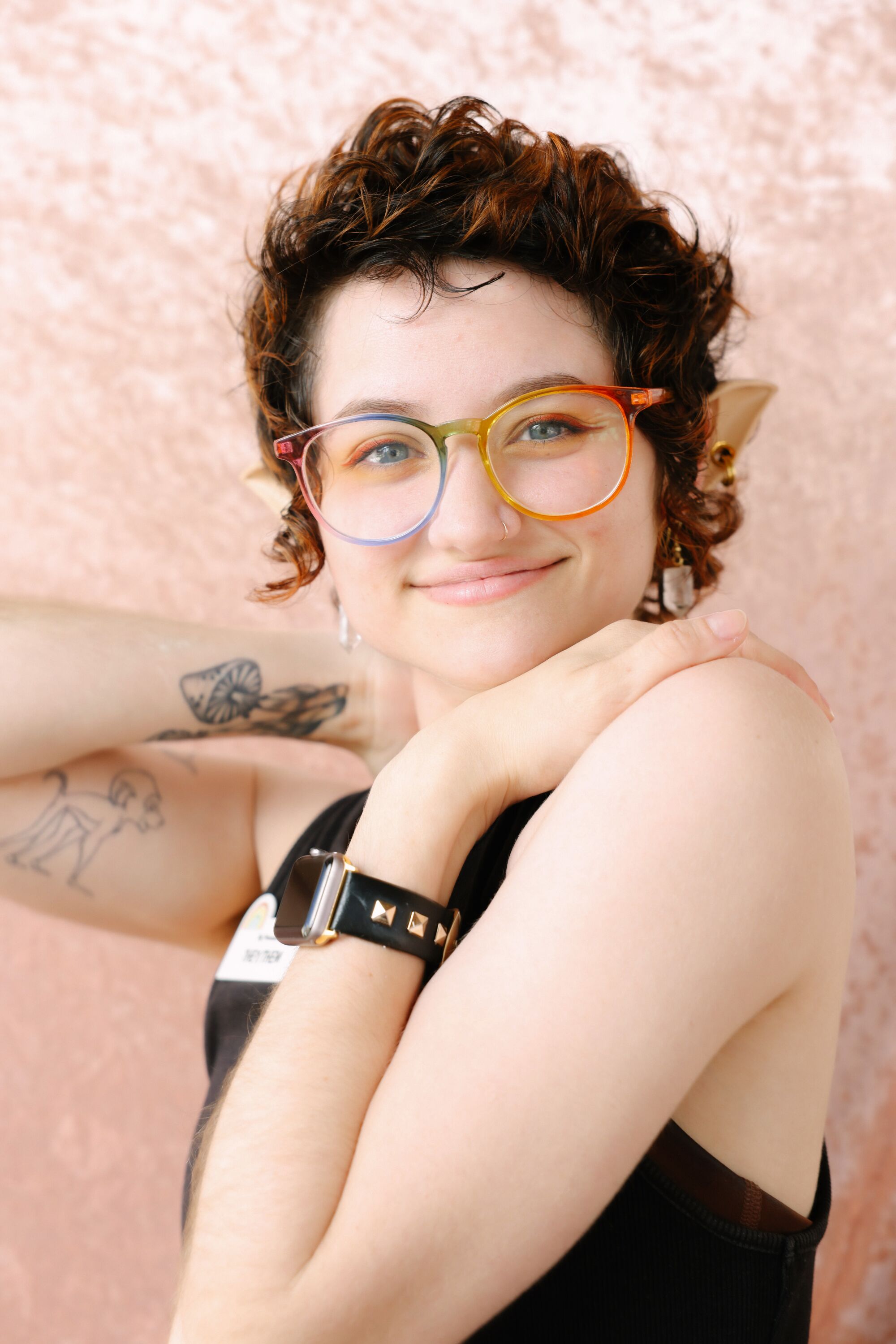 A person with rainbow glasses, elf ears and short hair poses for a portrait