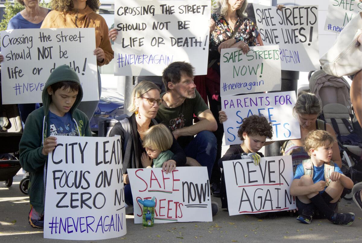 People hold signs saying "Safe streets now," "Never again," and "Crossing the street should not be life or death"