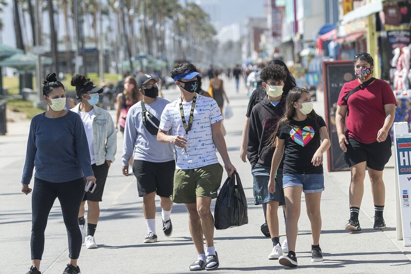VENICE, CA-MAY 14, 2020: People wear masks to protect against the coronavirus while walking along the boardwalk in Venice Beach. A new rule, announced by Mayor Eric Garcetti on Wednesday, now requires face masks for all outdoor activities. (Mel Melcon/Los Angeles Times)