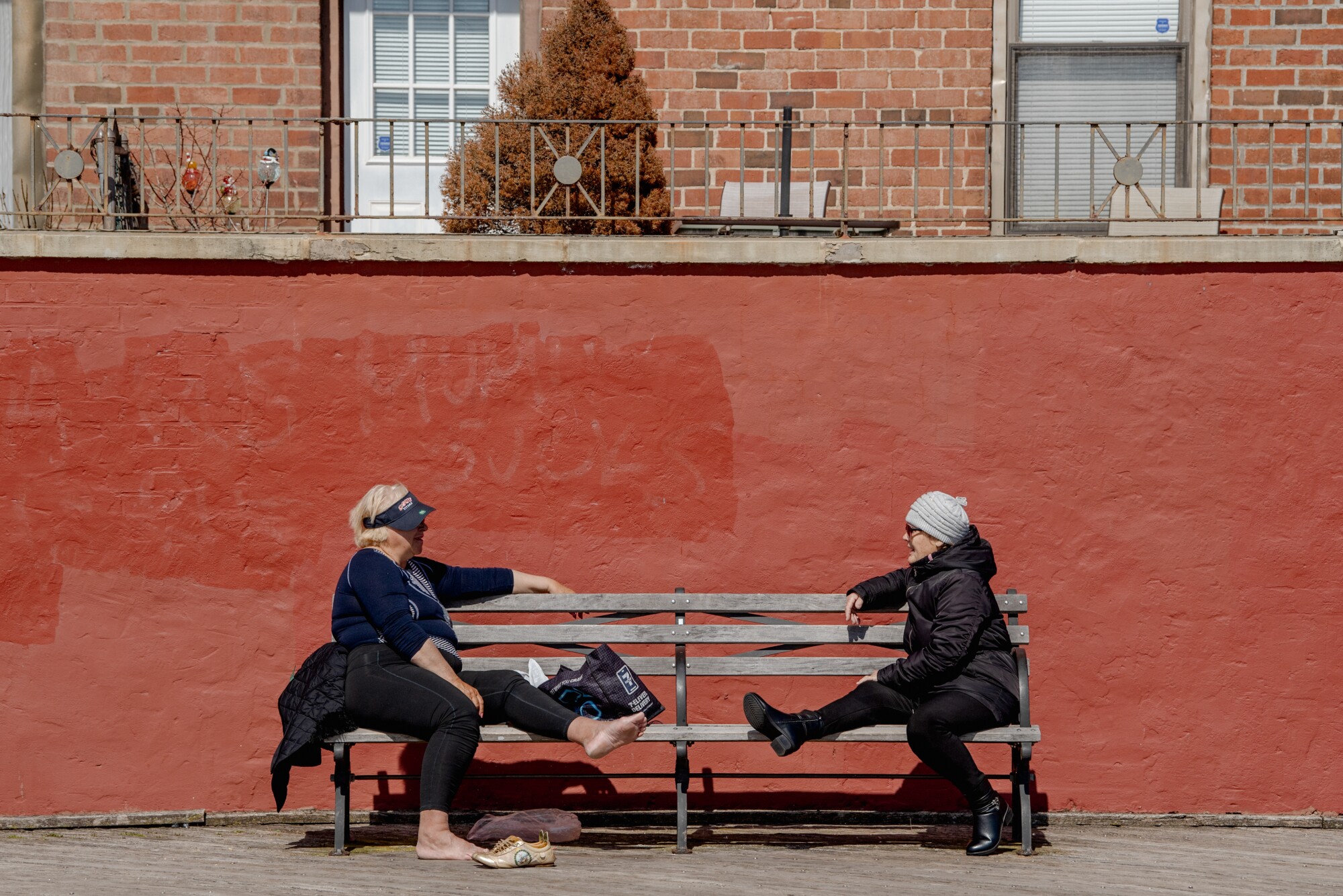 Two women talk on a bench with their legs stretched out.
