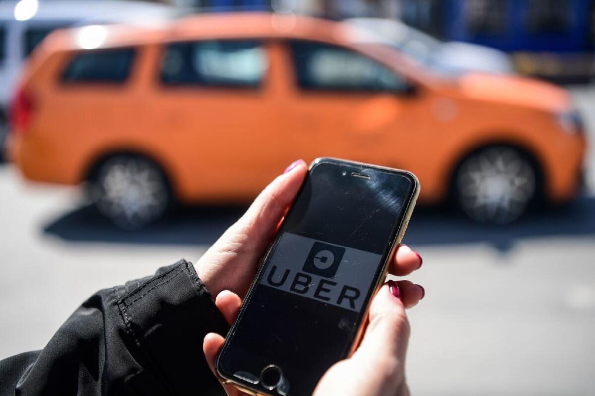 A person holds a cellphone with the Uber app on the screen.