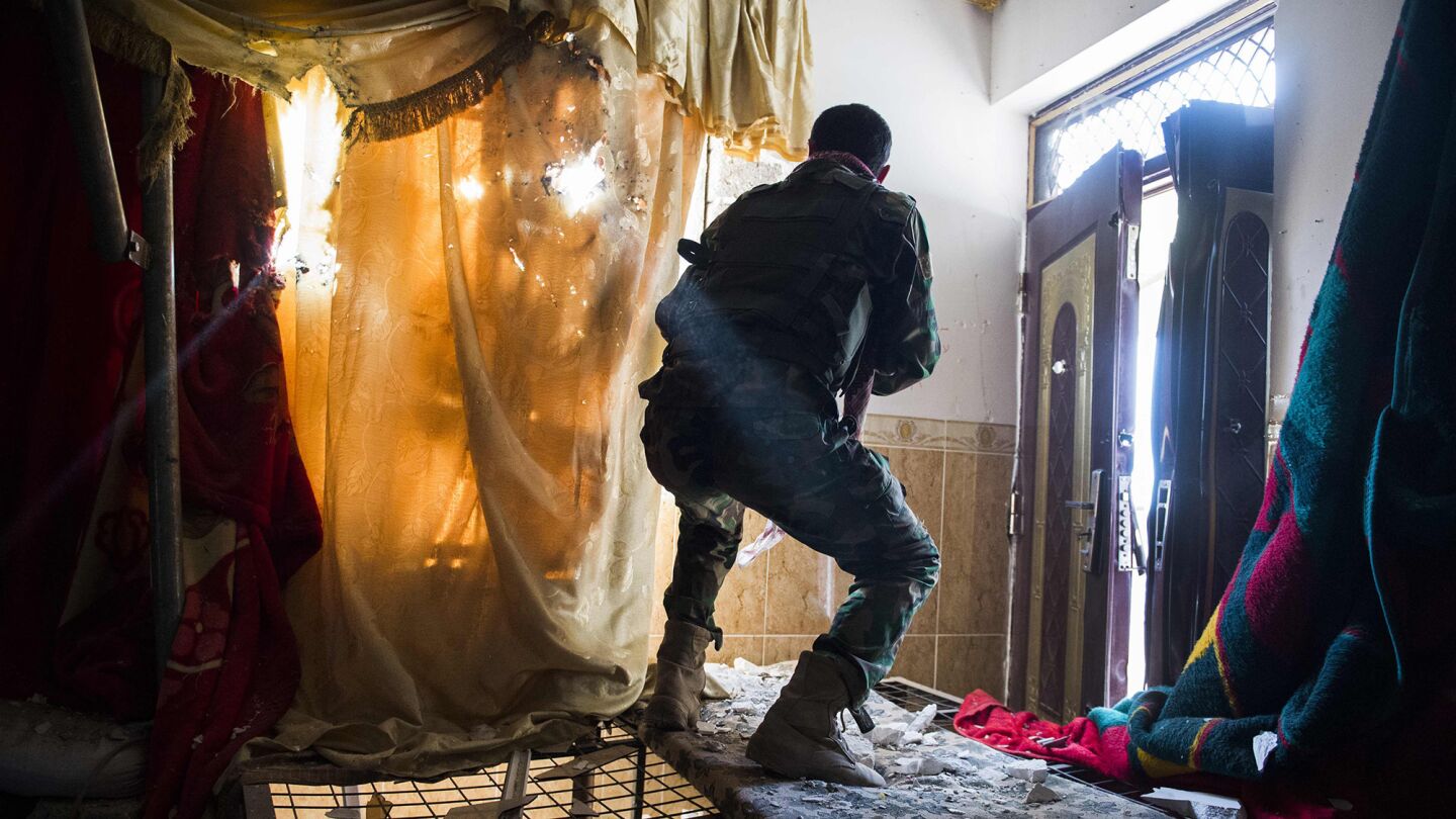 A peshmerga fighter peers through curtains as he and other Kurdish soldiers move into a new house in Bashiqa, Iraq, on Nov. 9.