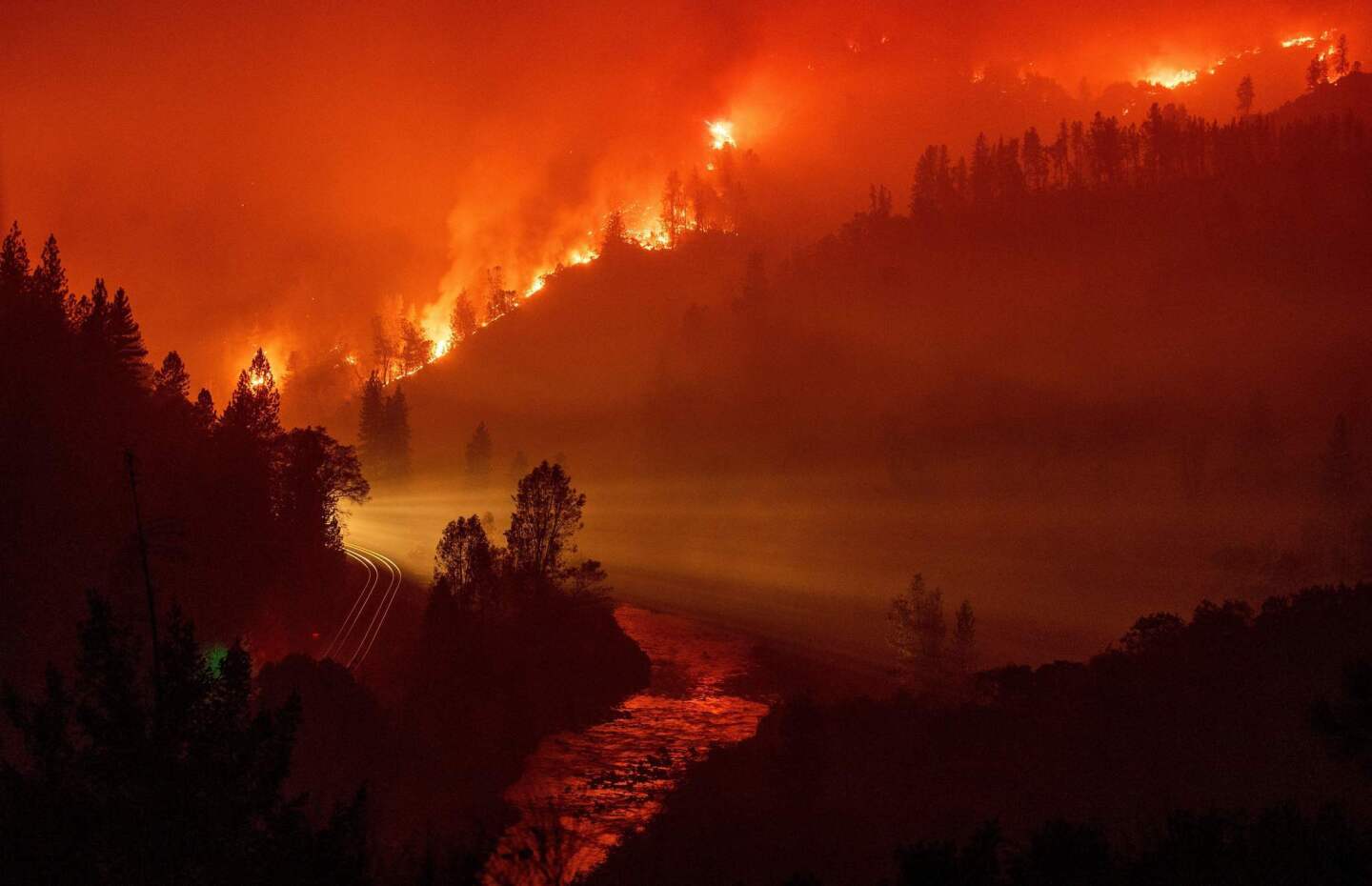Light from a train is seen as it rounds a bend near the Sacramento River as flames from the Delta fire fill a valley in Delta.
