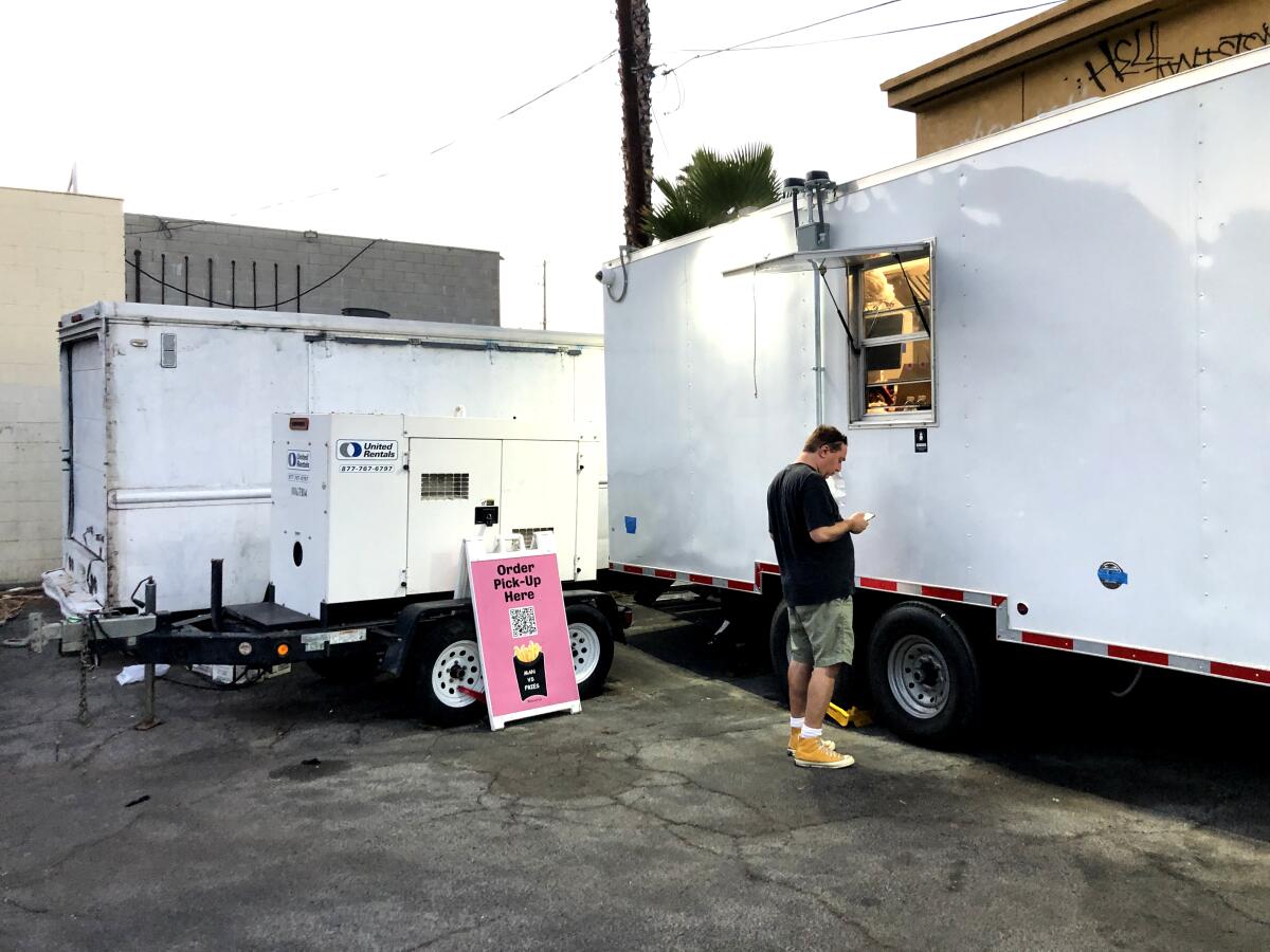 Sam Pocker stands in front of a white trailer with a window for food pickups