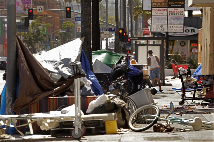 A homeless woman stands in the middle of an encampment on a sidewalk. 