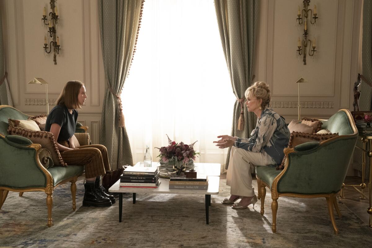 Two women sit on sofas across from each other in an ornate room.
