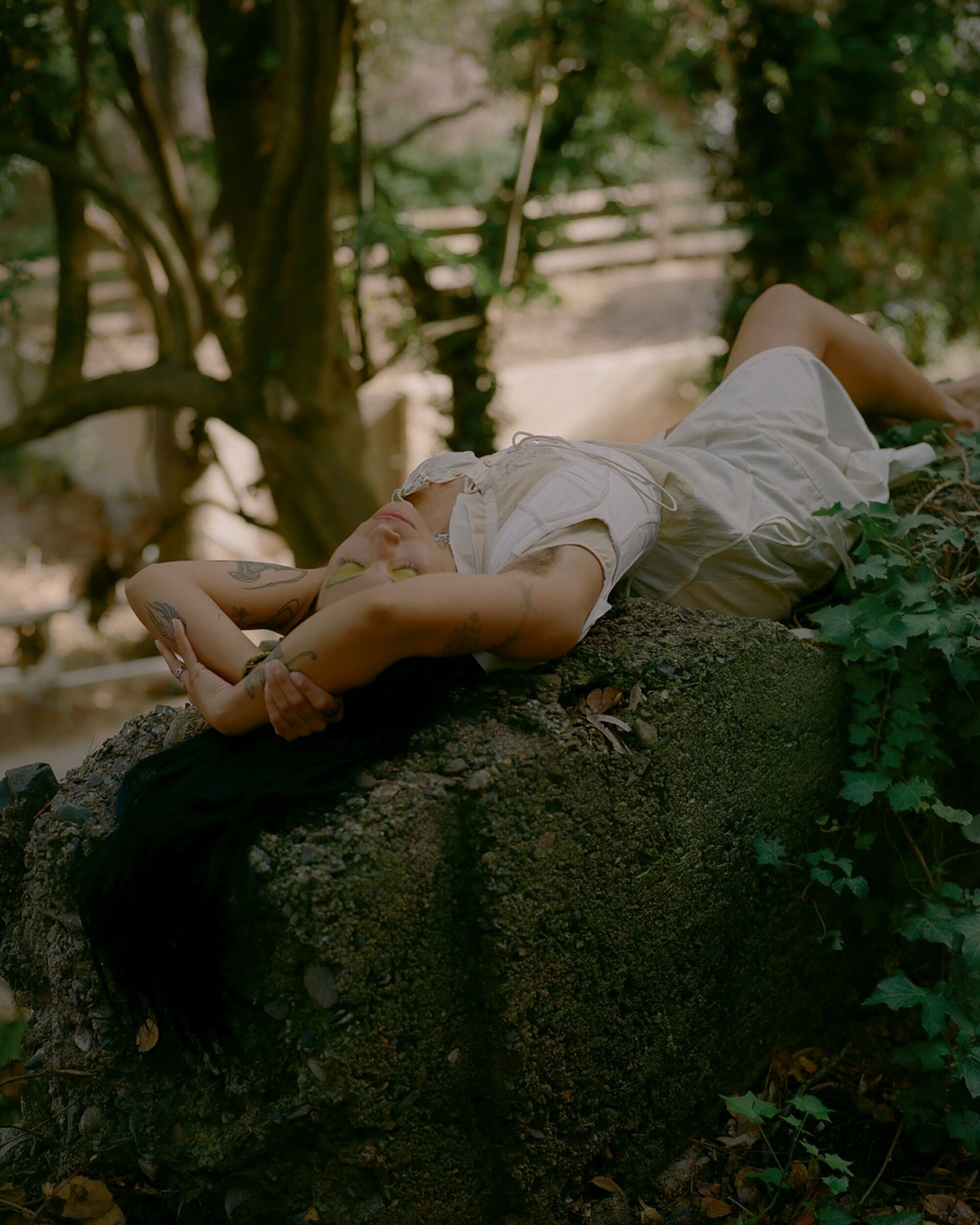 In a white dress, Mia Carucci lies on a concrete block outdoors.