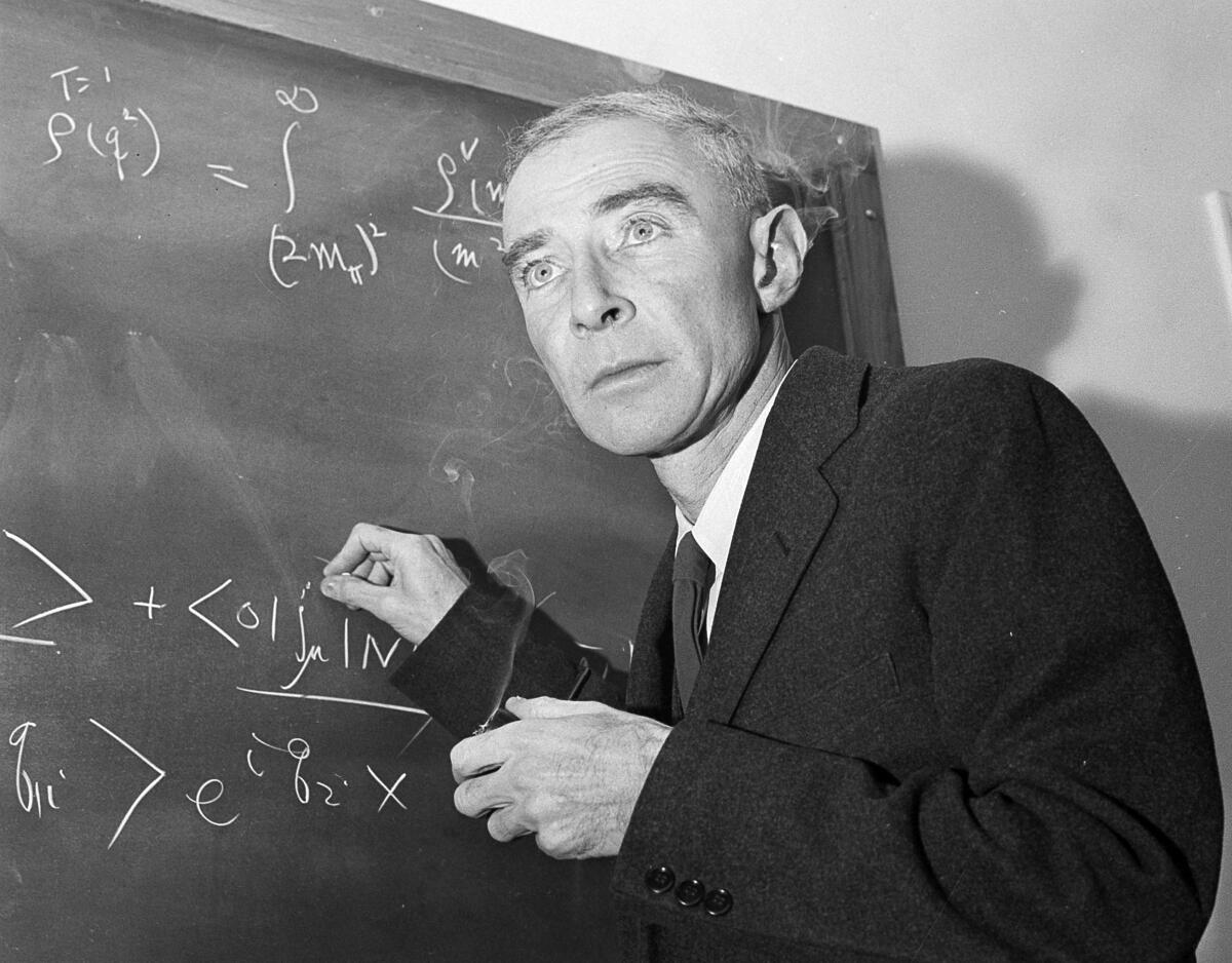 Robert Oppenheimer holds chalk as he writes on a chalkboard