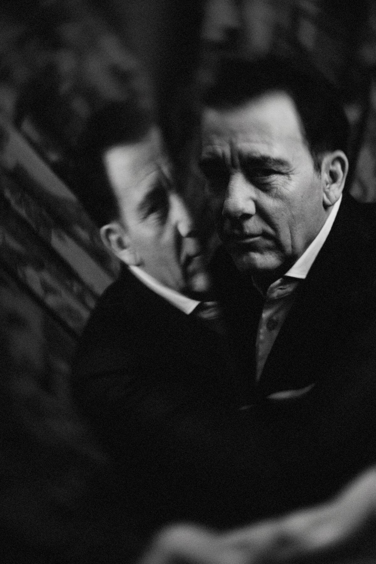 Clive Owen leaning against a reflection of himself.