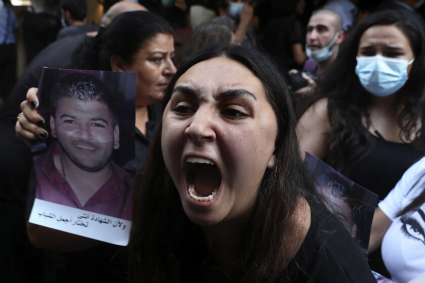 A woman whose brother was killed during last year's massive blast at Beirut's seaport, holds a portrait of him as she chants slogans during a protest outside the home of caretaker Interior Minister Mohamed Fehmi, in Beirut, Lebanon, Tuesday, July 13, 2021. Family members are angry with Fehmi because he rejected a request by the judge investigating the explosion to question Maj. Gen. Abbas Ibrahim, who is one of Lebanon's most prominent generals and heads of the General Security Directorate. (AP Photo/Bilal Hussein)