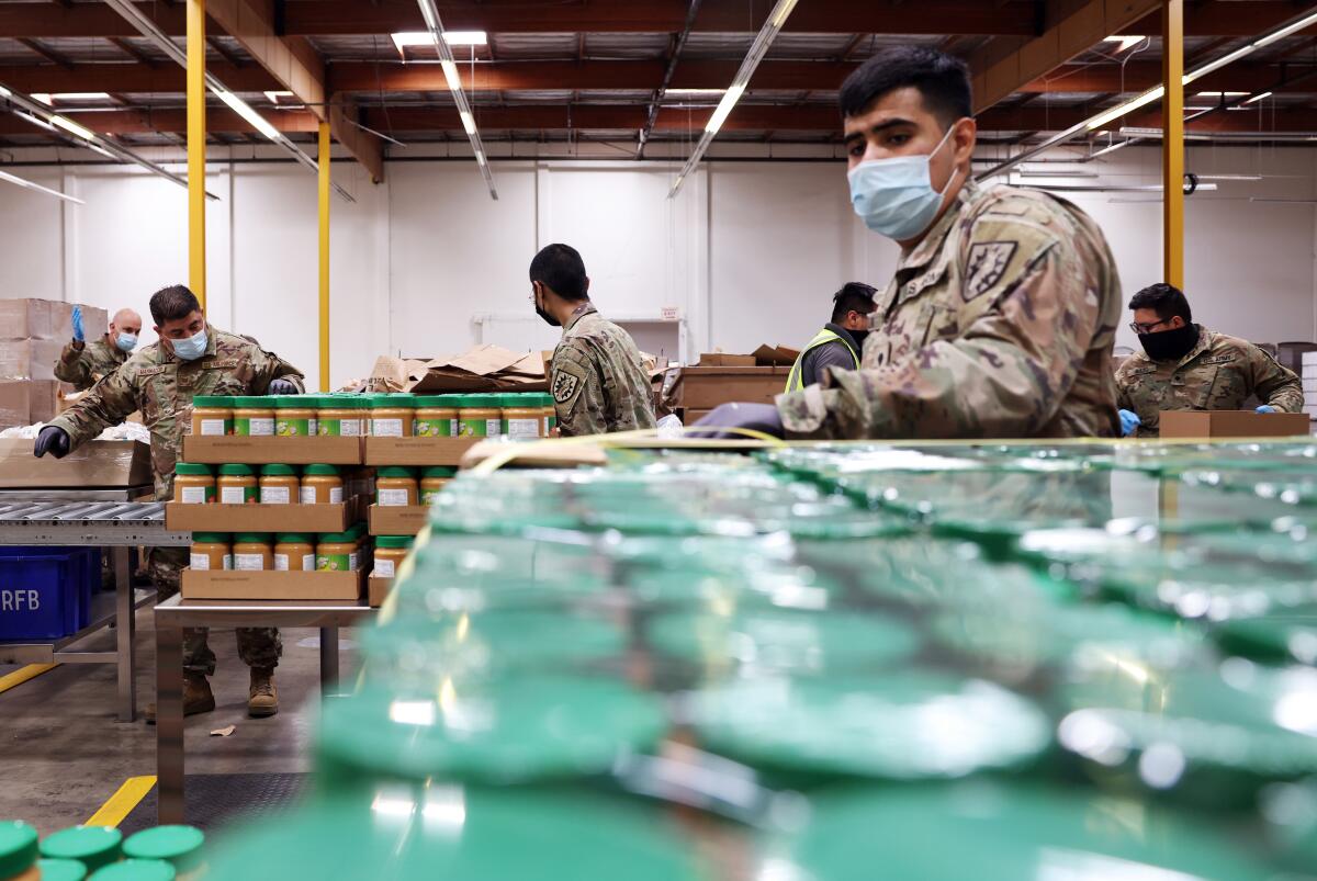 People in National Guard camo fatigues box up shelf-stable food in a warehouse