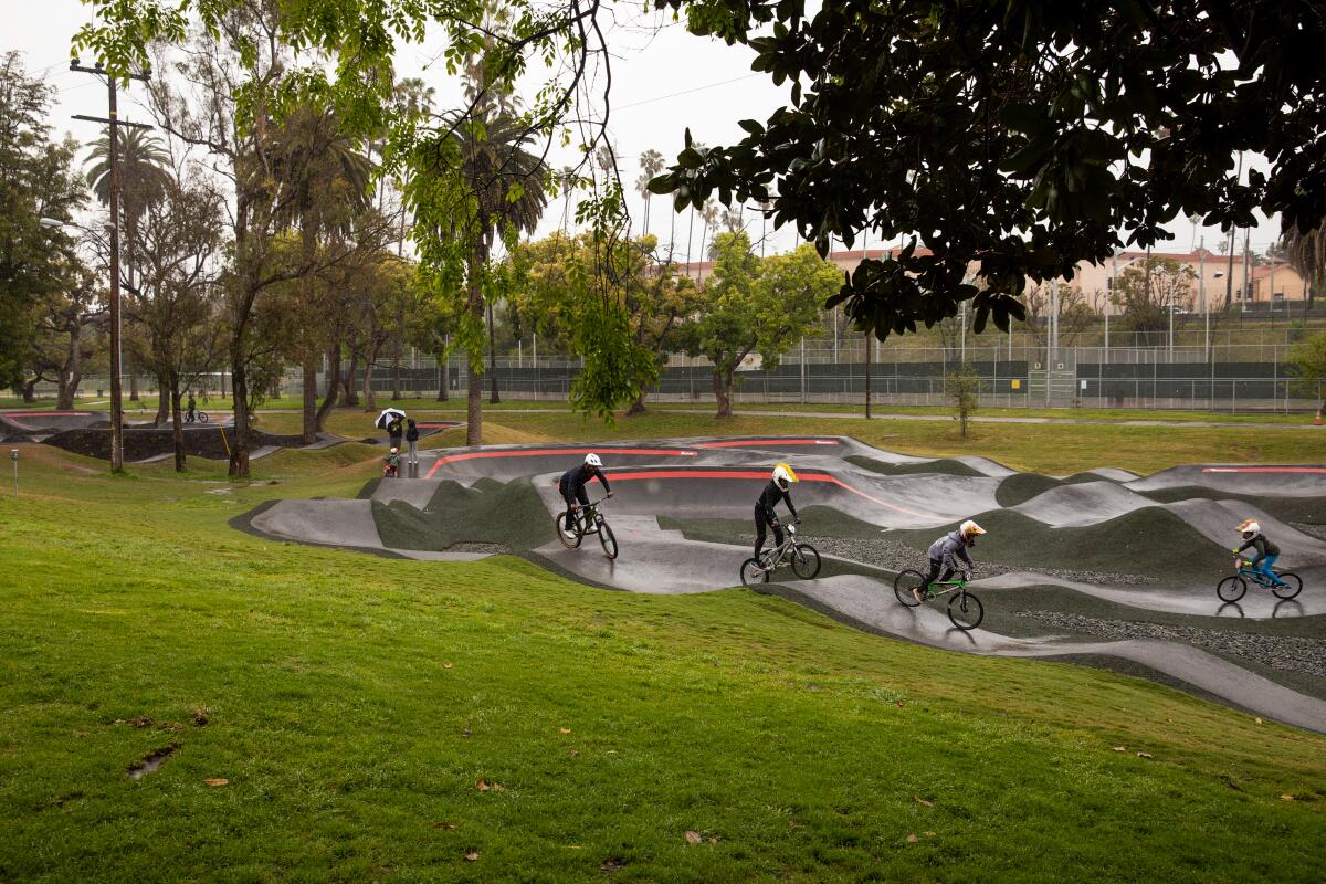 A group of bikers ride along a rainy pump track.